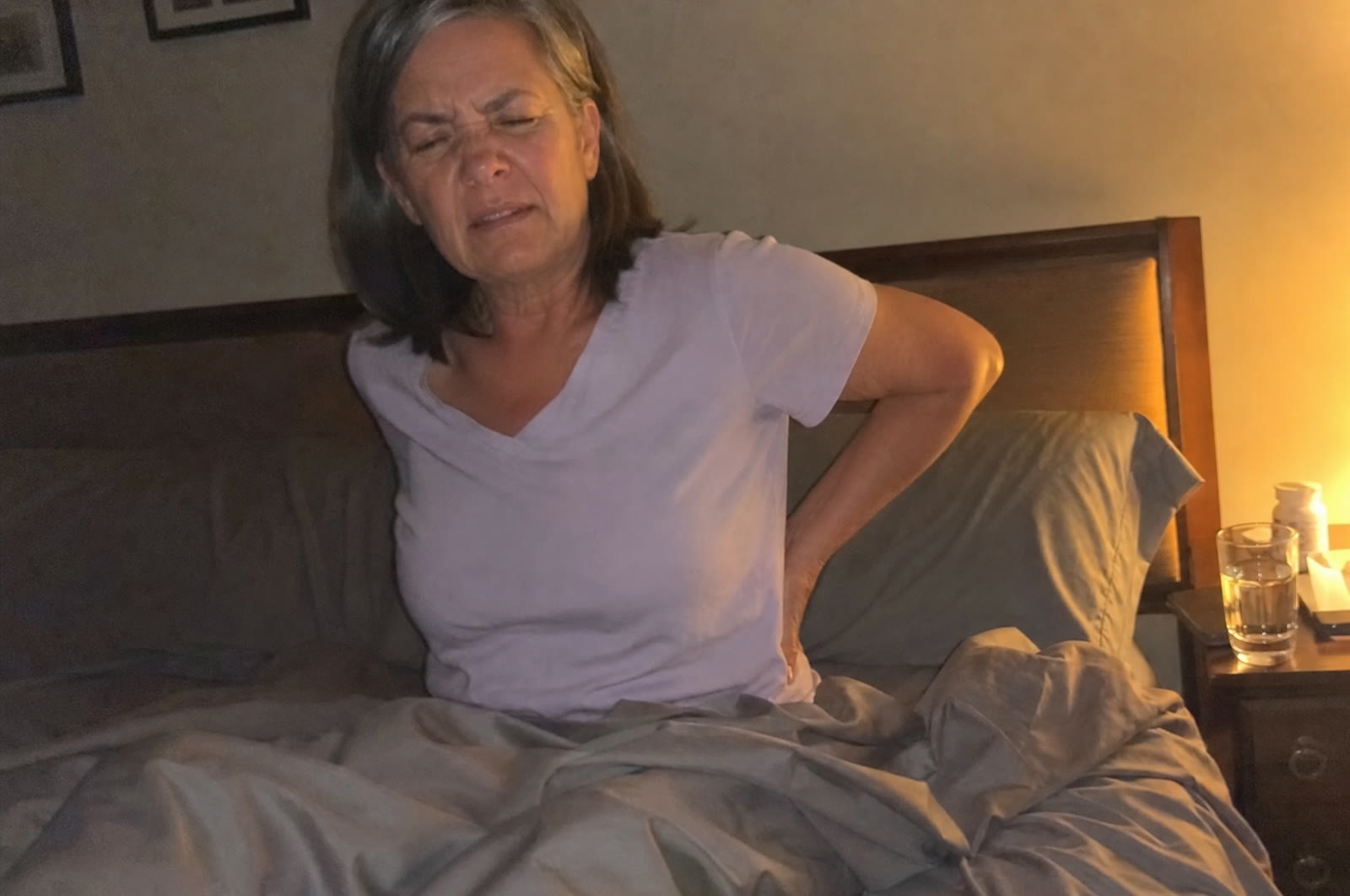 A woman in her 60s awake at night pressing her lower back in pain
