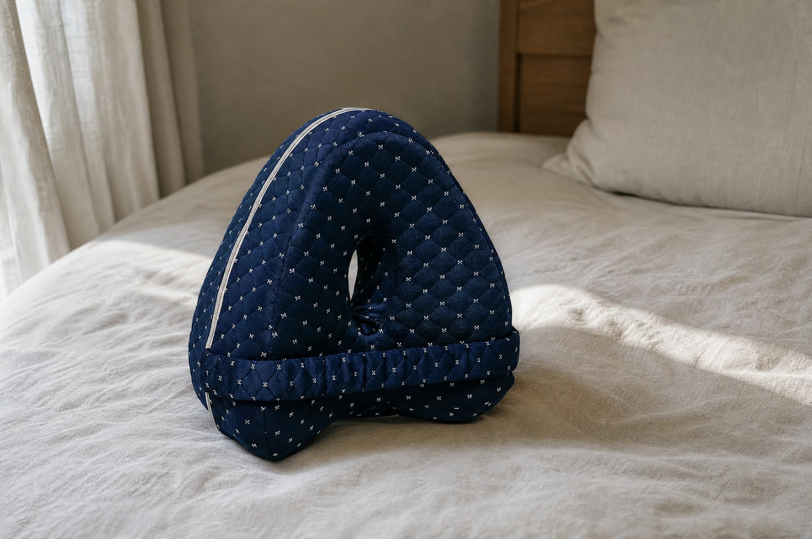 The Nourial Knee Alignment Pillow on a neatly made bed in morning light